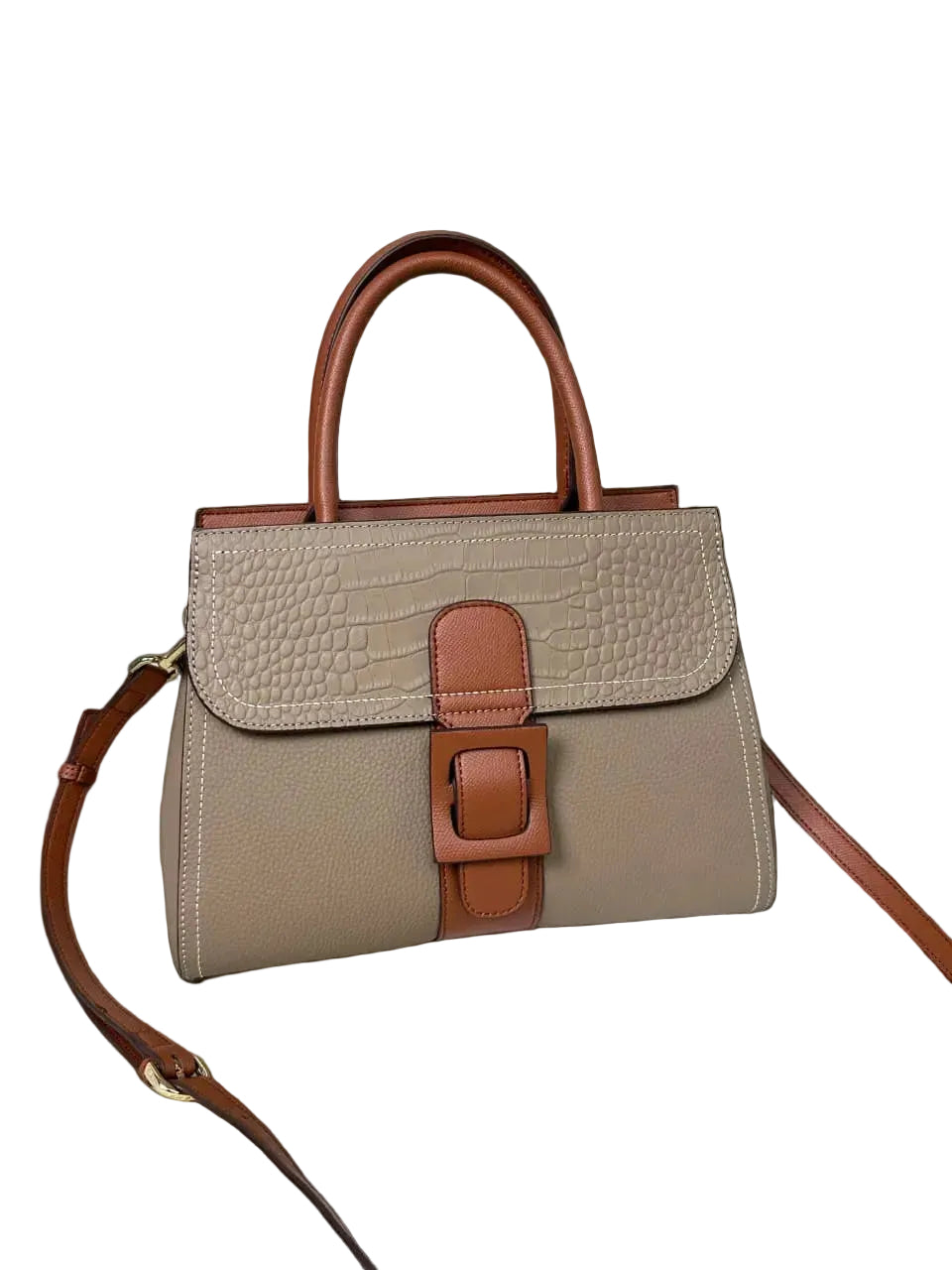 A structured handbag in taupe textured leather with brown leather handles, strap, and front buckle detail, displayed on a textured white surface with white curtains in the background.
