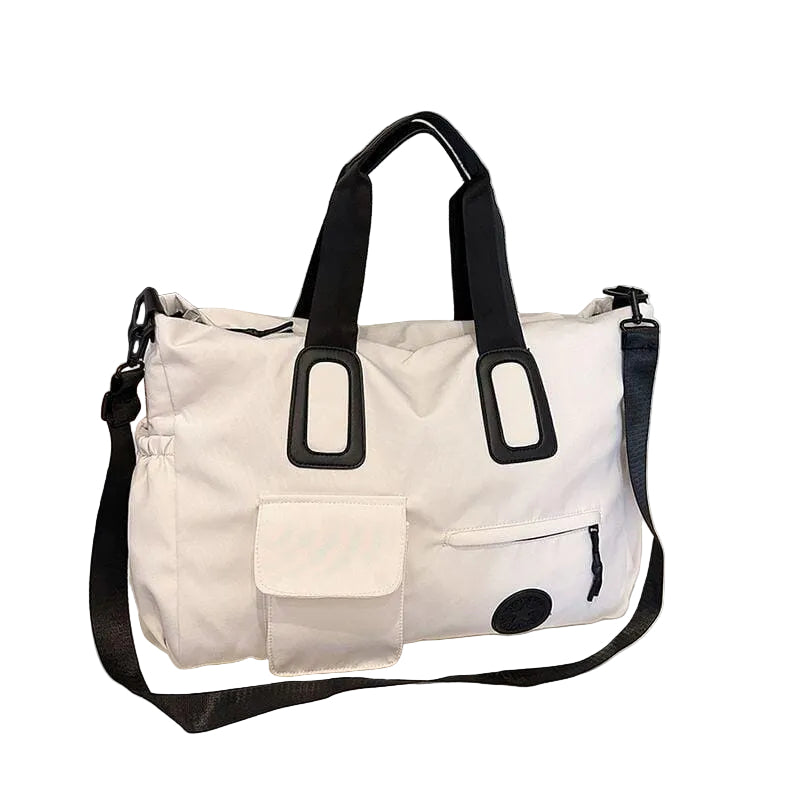 A white and black travel tote bag with dual top handles and a detachable shoulder strap, displayed on a tabletop in front of window blinds.