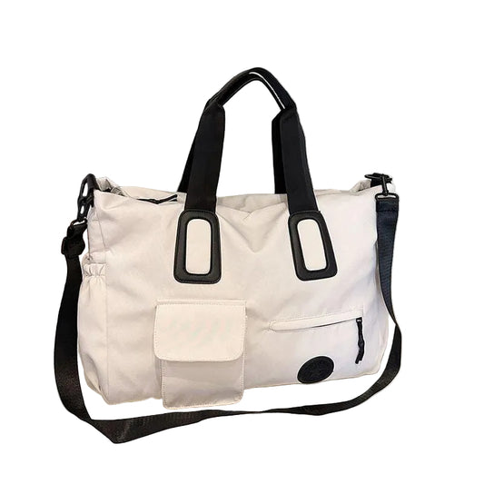 A white and black travel tote bag with dual top handles and a detachable shoulder strap, displayed on a tabletop in front of window blinds.