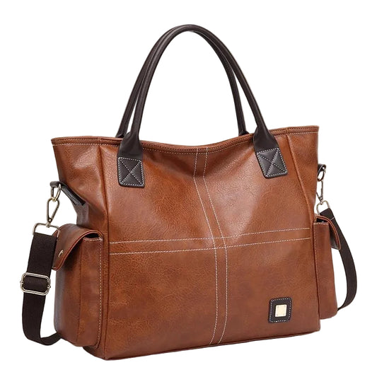 A brown faux-leather tote bag with black handles and a black shoulder strap, featuring white contrast stitching and a small square metal logo plate on the front, set against a solid light beige background.